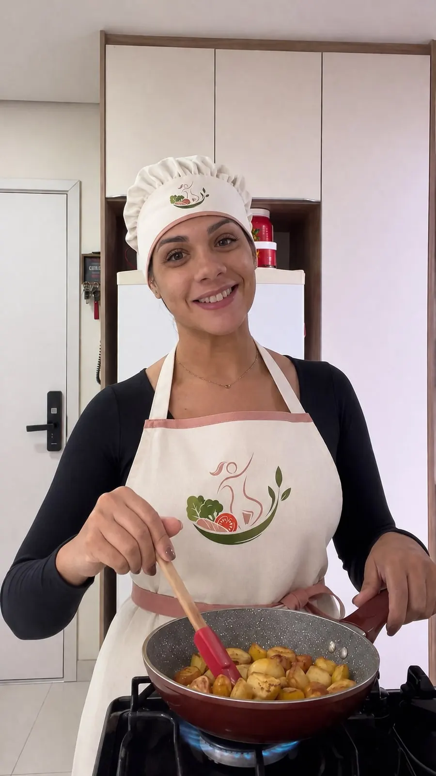 Jeniffer cozinhando, de avental da Fitfood by Jeni